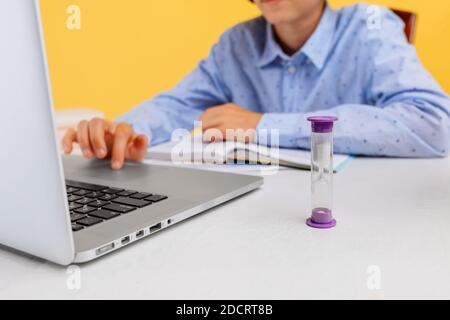 schoolboy sits at a Desk and uses a laptop, on a yellow background. Distance learning, quarantine, coronavirus Stock Photo