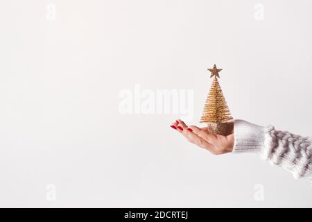 Female hand in white sweater holding golden Christmas tree with star, copy space. Stock Photo