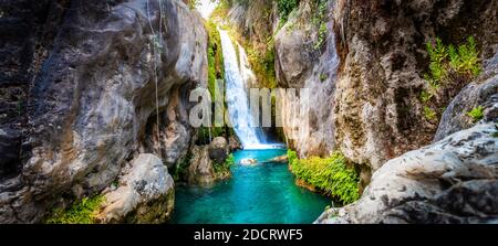 A great waterfall between the rocks with cold clear water in shades of blue and green on a beautiful summer day. Stock Photo