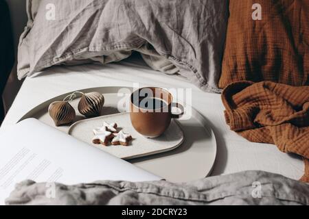 Winter festive still life. Cup of coffee, Christmas paper ornaments and magazine. Star gingerbread cookies on beige tray. Breakfast in bed. Linen and Stock Photo