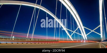light traces of cars driving along the road at night through a beautiful modern highway bridge Stock Photo