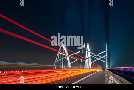 light traces of cars driving along the road at night through a beautiful modern highway bridge Stock Photo