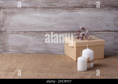 mock up of two white candles in a jute rope and beige gift box, cones on a wooden background Stock Photo