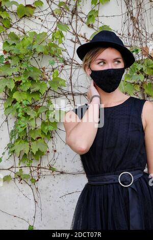 Young girl with black hat, black dress and mask for the COVID Stock Photo