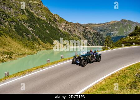 A vintage car Alvis Speed 20 Special driving past a lake on Silvretta Hochalpenstrasse during the Arlberg Classic Car Rally. Stock Photo