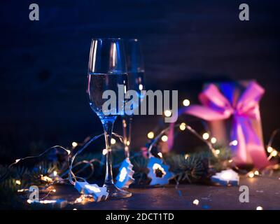 Celebrate Christmas, two glasses of sparkling champagne at night on a table lit with garlands and colored lights Stock Photo