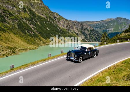 A vintage car Bentley Mk VI Graber Coupe driving past a lake on Silvretta Hochalpenstrasse during the Arlberg Classic Car Rally. Stock Photo