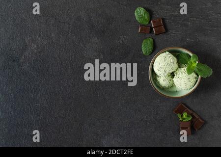 Scoops of mint ice cream with chocolate crumbs in a plate on black background top view. Summer refreshing dessert. Stock Photo