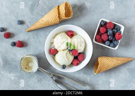 Vanilla ice cream scoops with raspberry and blueberry in a bowl top view on grey background. Refreshing summer dessert. Stock Photo