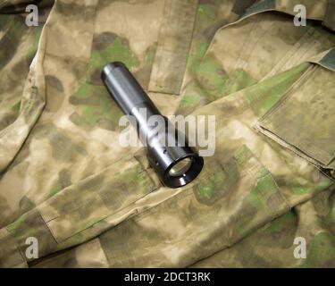 a black flashlight lies on a military camouflage jacket Stock Photo