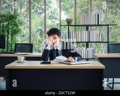 Young Asian businessman receiving bad news with dismissal letter, tired, stressed and sad sitting with absent-minded on his desk in office. Frustrated Stock Photo