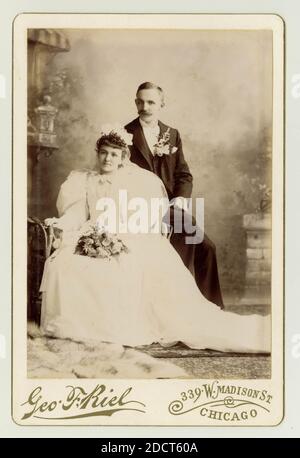Original late 19th century cabinet card studio portrait of wedding couple, The woman is wearing a white dress with big 'leg of mutton' puffed sleeves. Photo by Geo,. F. Riel, at 339 W. Madison St. Chicago, U.S.A. circa 1895