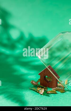 Miniature wooden house in glass dome on green background. Dream house concept, real estate investment. Property insurance. Selective focus Stock Photo