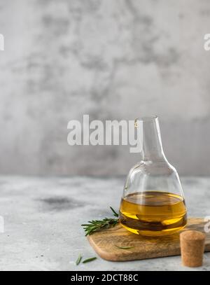 glass bottle of extra virgin olive oil with a branch of rosemary. gray background, vertical image Stock Photo