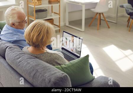 Older couple is sitting at home in the living room and talking to their family doctor via video link Stock Photo