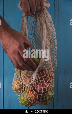 Male hand picking the green apple from cotton mesh eco bag with fruits. Vegan, eco friendly, zero waste, reusable concept Stock Photo