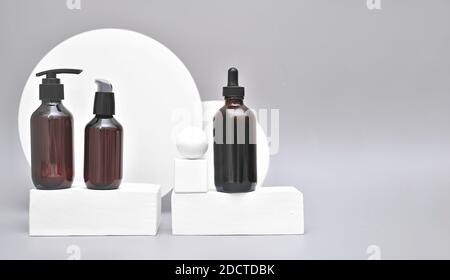 unbranded cosmetic bottles on white podium or pedestal. brown dispenser bottles with cosmetic cream or lotion. self care spa concept. minimal trendy geometric style composition.copy space for text. Stock Photo