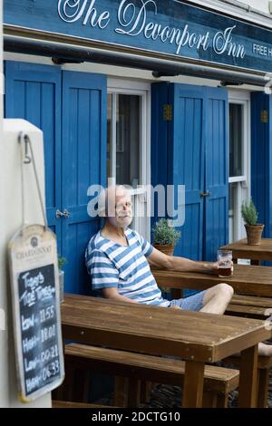 Happy man wearing a breton striped shirt sitting outside a pub drinking a pint in Kingsand ,Cornwall , UK Stock Photo