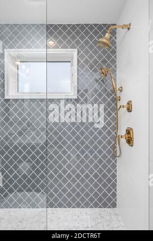 A remodeled shower with beautiful grey tiles on the wall, marble polygon tiles on the floor, and a gold shower faucet set. Stock Photo