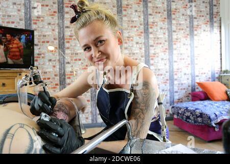 A female tattoo artist applying her craft onto the back and arm of a man . Stock Photo