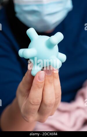 Close-up of sick woman model wearing surgical or medical disposable protective mask showing fake plastic coronavirus replica as covid19 sars influenza Stock Photo