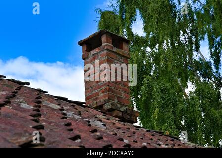 Classic old brick chimney looking weathered and old. Sitting on a roof of red clay tiles. Stock Photo