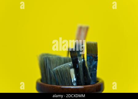 Used paint brushes sitting in a jar and isolated on yellow background Stock Photo