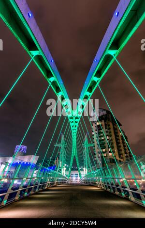 Illuminated vibrant steel cable-stayed suspension bridge at The Lowry in Salford Quays, Greater Manchester, UK. Stock Photo