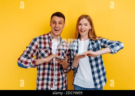 Young successful couple, man and woman spend money throwing banknotes, on yellow background Stock Photo