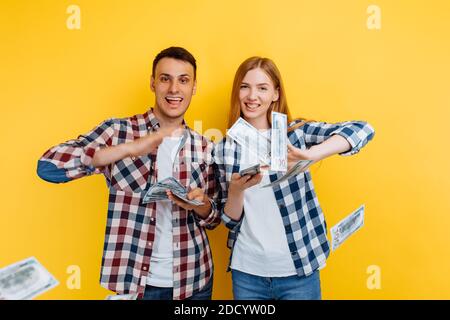 Young successful couple, man and woman spend money throwing banknotes, on yellow background Stock Photo