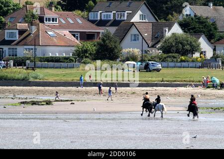 Maidens Harbour, South Ayrshire, Scotland, UK . Maidens is a village in the Kirkoswald parish of Ayrshire, Scotland. Situated on the coast of the Firth of Clyde at the southern end of Maidenhead Bay, a series of rocks known as the 'Maidens of Turnberry' form a natural harbour.  From the harbour looking across to the beach horse riders and family picnic Stock Photo