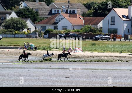 Maidens Harbour, South Ayrshire, Scotland, UK . Maidens is a village in the Kirkoswald parish of Ayrshire, Scotland. Situated on the coast of the Firth of Clyde at the southern end of Maidenhead Bay, a series of rocks known as the 'Maidens of Turnberry' form a natural harbour.  From the harbour looking across to the beach horse riders and family picnic Stock Photo