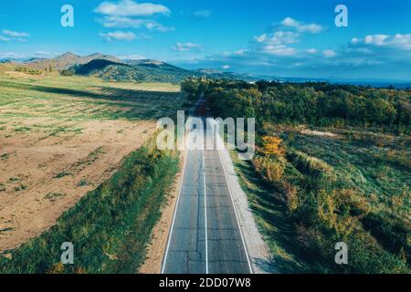 Empty asphalt road or route, or way in mountain countryside among green meadows and forest as idea of freedom and travel. Stock Photo
