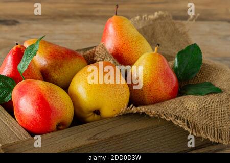 ripe red and yellow pears in a wooden box close-up. background with ripe pears and green leaves Stock Photo