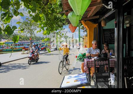 A Vietnamese woman wearing a tradition conical hat and riding a bicycle on Bach Dang Street, Hoi An, Vietnam, Asia Stock Photo