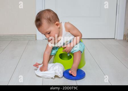 potty training concept. A cute little baby sits on a green pot and plays with a diaper in the room. close-up, soft focus, place for copy space. Stock Photo
