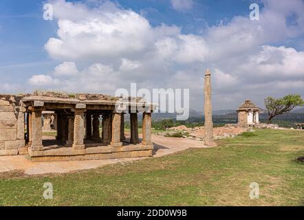 Hampi, Karnataka, India - November 4, 2013: Ruins at Moola Virupaksha temple behind green lawn and under blue cloudscape. Stock Photo