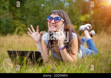 young woman emotionally talking on the phone in front of laptop Stock Photo