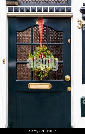 Christmas wreath on entrance vintage door outside. Veranda front door decorated by christmas festive wreath decor. Traditional Christmas exterior in Stock Photo