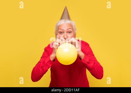 Senior hispanic woman celebrating her birthday. Studio shot on yellow wall. Stock Photo