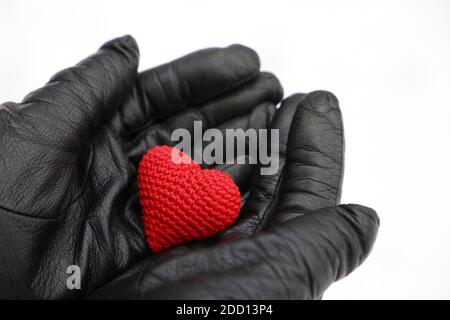 Red knitted heart in female hands in black leather gloves on snow background. Concept of romantic love, Valentine's day, health care at winter Stock Photo