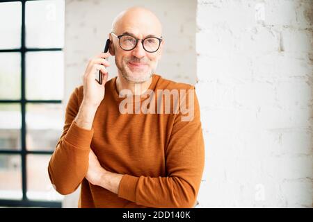 Portrait shot casual man talking with somebody on his mobile phone while standing by the window. Stock Photo