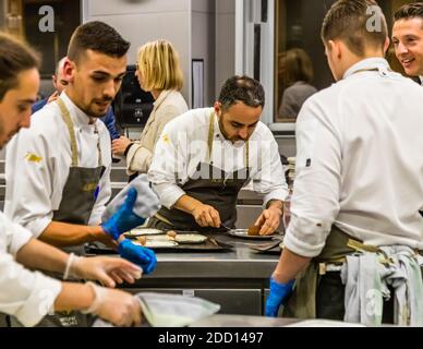 The kitchen team at the Hotel Alàbriga plates several dishes in Sant Feliu de Guíxols, Spain. The chef working at the centre is possibly head chef Abraham Artigas; food journalist Angela Berg watches in the background. Stock Photo