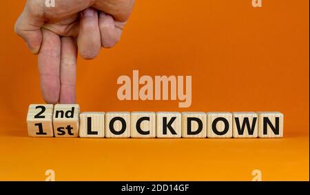 Symbol for a second lockdown. Hand turns cubes and changes the expression '1st lockdown' to '2nd lockdown'. Beautiful orange background. Medical and c Stock Photo