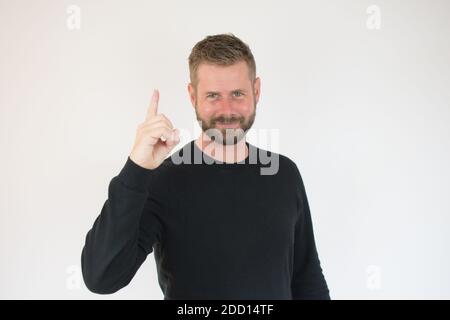 Attractive young man in black sweater pointing up with his finger isolated on white background Stock Photo