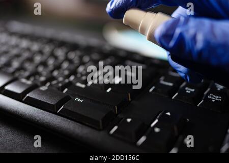 Hand in protective glove with alcohol spray cleaning keyboard. Covid-19 disinfection concept. Stock Photo