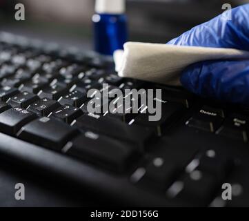 Hand in protective glove with napkin cleaning keyboard. Covid-19 disinfection concept. Stock Photo