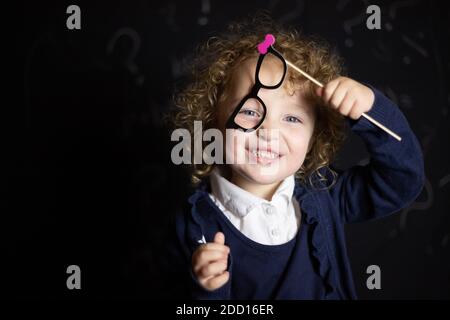 child toddler 3 year old dressed as a teacher and thinking with chalk board and question marks, child teacher glasses cute, think, chalk board Stock Photo
