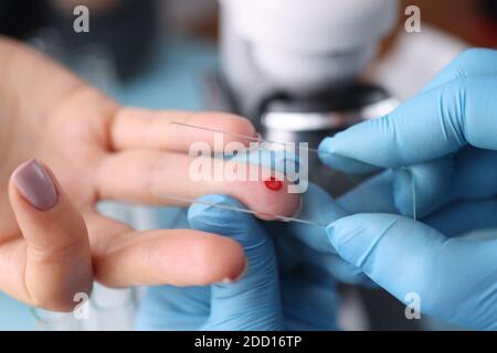 Doctor in protective gloves touching drop of blood on patients hand with specimen slide Stock Photo