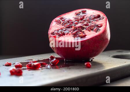 Fresh cut pomegranate on dark cutting board with seeds and juice on board Stock Photo